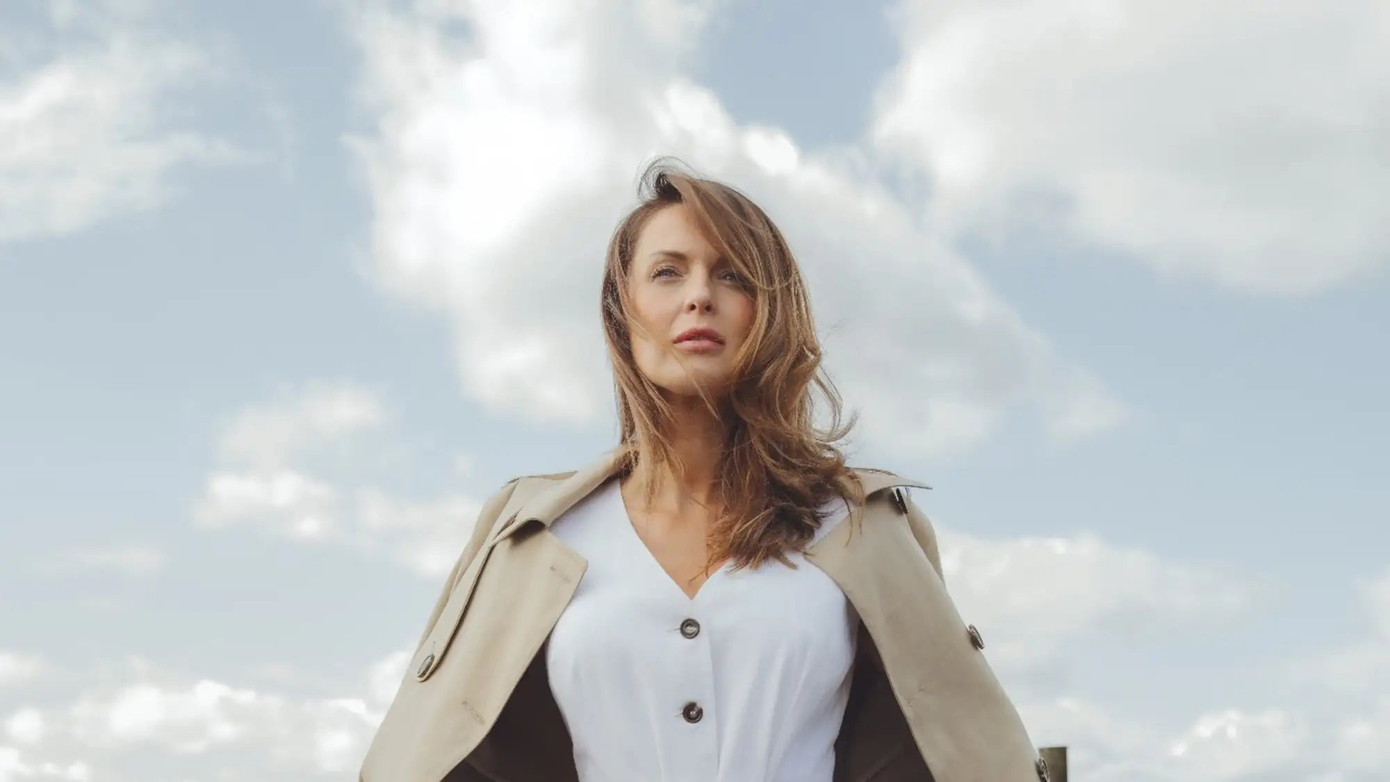 A woman wearing a beige trench coat over a white button-up shirt.