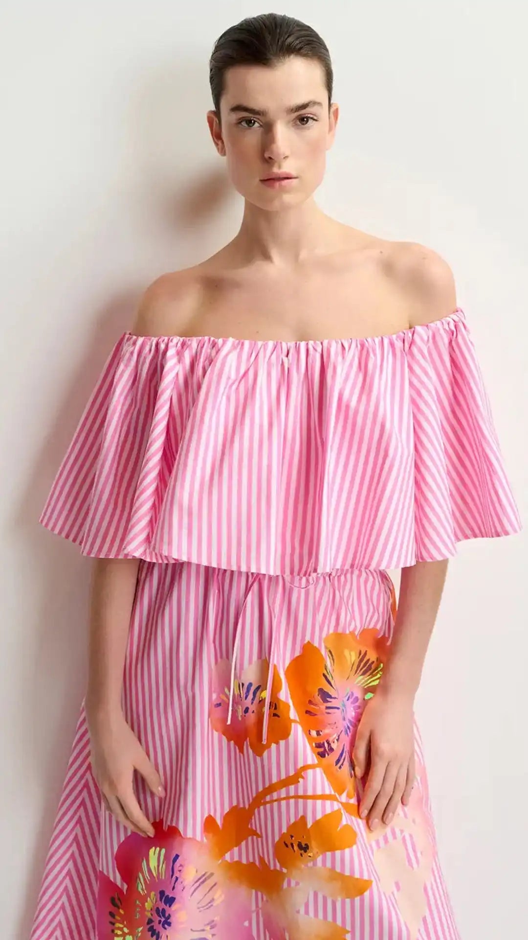 A woman wearing a pink and white striped off-the-shoulder dress with a floral pattern on the skirt.